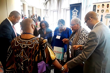 The Rev. Jacqui King (second from right) clasps hands and prays with people at the Discipleship Ministries booth during the 2019 meeting of Black Methodists for Church Renewal in Atlanta. Photo courtesy of King.
