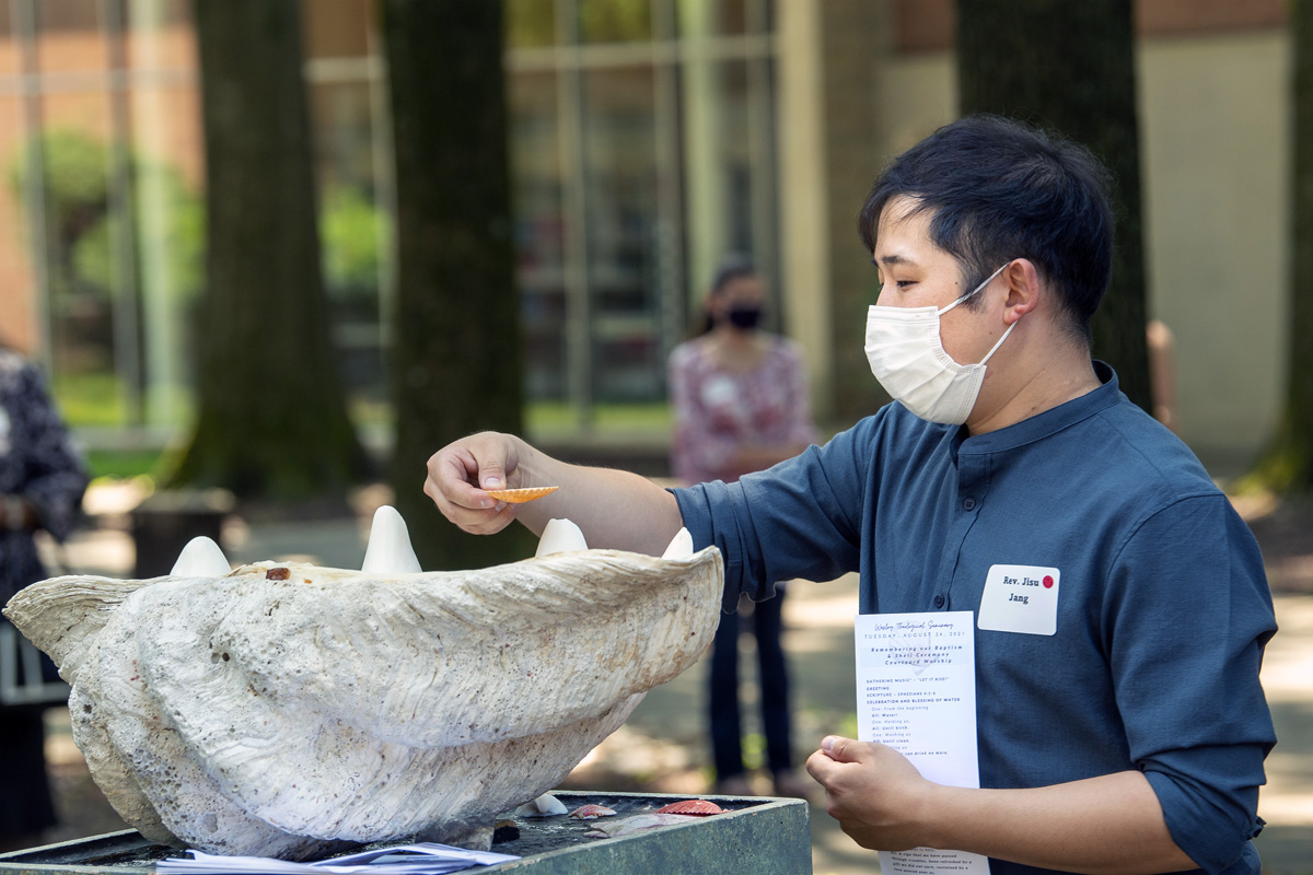 The Rev. Jisu Jang dips a shell into water during an Aug. 24 Renewal of Baptism and Shell Service at Wesley Theological Seminary in Washington. The service uses shells as a symbol of students’ journey of faith and ministry. Wesley is resuming on-campus gatherings, albeit with vaccination and mask mandates, after a long period of remote learning due to the pandemic. Photo by Lisa Helfert Photography for Wesley Theological Seminary, 2021.