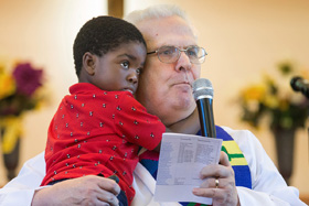 The Rev. Bill Jenkins preaches during worship at Exodus United Methodist Church in San Diego in 2018 while holding his son Harry, who is from Haiti. File photo by Mike DuBose, UMNS.