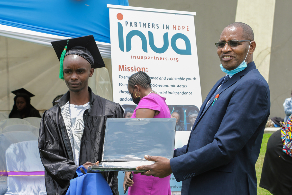 The Rev. Paul Matheri (right), program director for Inua Partners in Hope and district superintendent in Naivasha, Kenya, issues a laptop to a graduate during a graduation ceremony in September. The vocational program provides orphans and vulnerable young people with hands-on job skills and startup kits or capital in their fields of specialty. Photo by Gad Maiga, UM News.