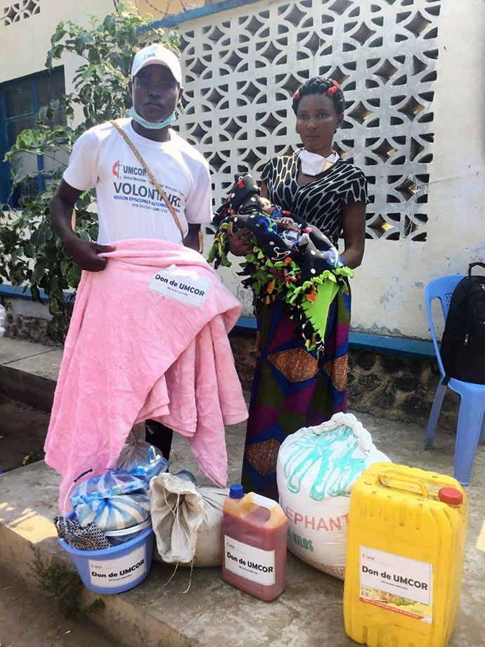 Madame Ortance Tshikonga 38 ans et l'un des volontaires qui l’a aidé à transporter ses vivres et non vivres après la réception. Tshikonga  est veuve et Mère de quatre enfants. Plus de 415 familles constituées de plus de 2 490 personnes expulsées de l’Angola, ont bénéficié de la nourriture et vêtements, une assistance de l’Eglise Méthodiste Unie. Photo du Pasteur Serge Mukendi, UM News.