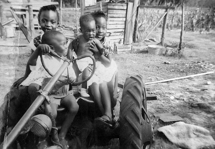 James Salley senta-se na cadeira do motorista de um tractor quando criança em 1957, cercado por três de suas irmãs. Salley, que cresceu na fazenda de sua família no Condado de Allendale, SC, estabeleceu uma bolsa de estudos na África University em homenagem a seus pais batalhadores, Marie e James Salley. Foto de cortesia de James Salley.