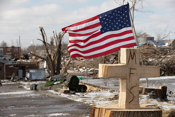A U.S. flag and a cross carved from a tree stump form a makeshift memorial in Mayfield, where a tornado devastated much of the downtown area. The initials in the cross stand for “Mayfield Strong,” a motto adopted after the storm, which killed 22 people in Mayfield and surrounding Graves County. Photo by Mike Dubose, UM News.