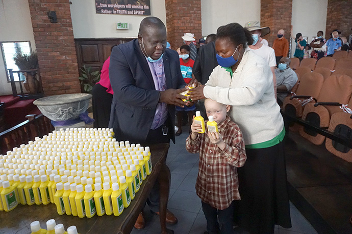 The Rev. Oscar Nyasha Mukahanana offers bottles of sunscreen to Simba Tembo and his mother, Dorika, during a program at Cranborne United Methodist Church in Harare to help support people living with albinism. Mukahanana is superintendent of the church’s Harare East District. Photo by Kudzai Chingwe, UM News.