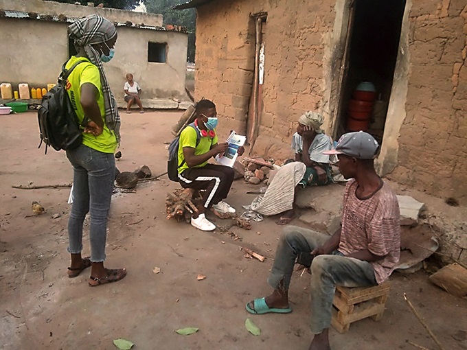 Jóvenes voluntarios/as de la IMU del Este de Angola, con camisetas INM verde claro, hablan con personas de la comunidad y se reúnen con ellos/as en sus puertas para explicarles formas de prevenir la malaria. Foto de C. Salvador.
