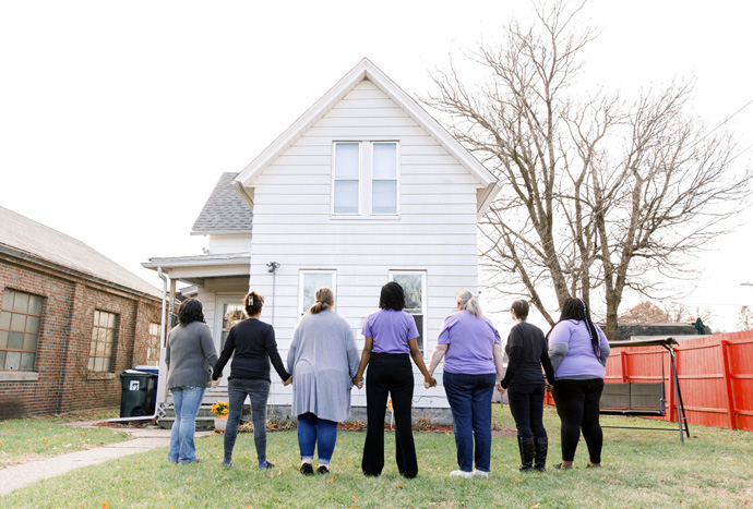 Kit Evans-Ford and survivors hold hands in front of Argrow’s House for Healing and Hope in Davenport, Iowa. The social enterprise, which makes and sells bath and body products, was founded to provide a safe place for women healing from domestic abuse to make a living wage. Photo courtesy of Kit Evans-Ford.
