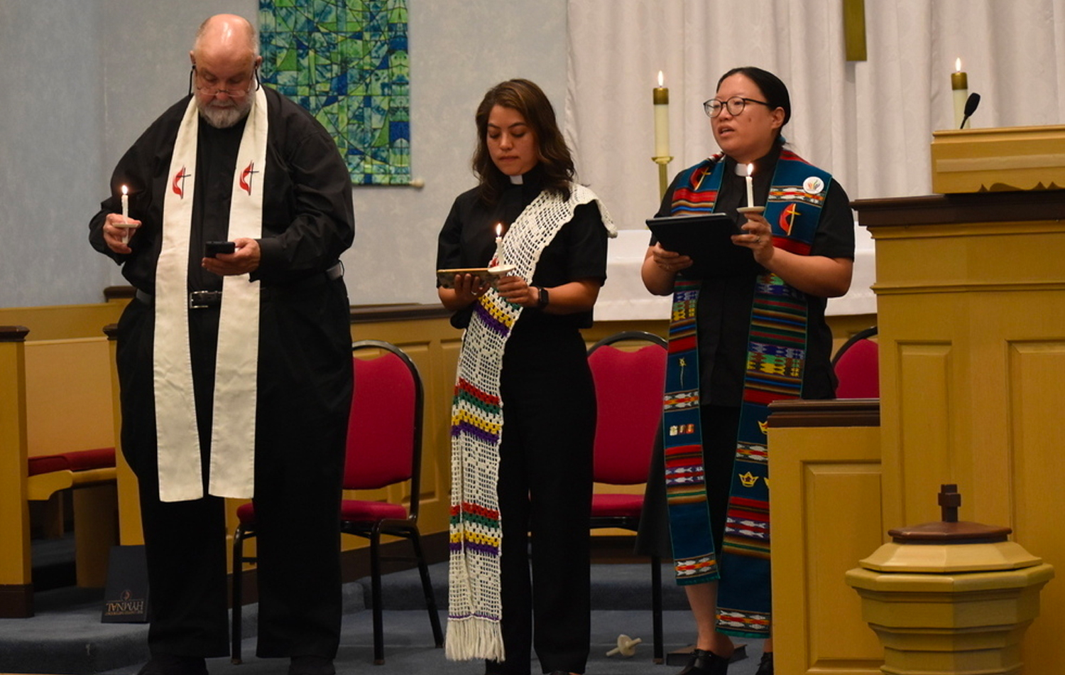 Durante una vigilia de oración el 5 de julio, el Rev. Cal Haines de Lake Bluff, la Diácona Patricia Bonilla de la IMU Grace y la Revda. Esther Lee de la IMU Cristo en Deerfield, sostienen velas y recuerdan a las víctimas y los/as heridos/as en el desfile del 4 de julio en Highland Park. Foto cortesía de la Conferencia Anual del Norte de Illinois.