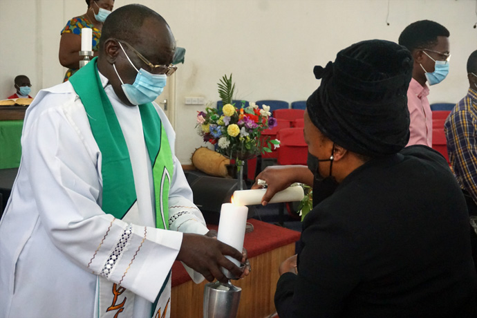 The Rev Daniel Mutidzawanda, lead pastor of Chisipiti United Methodist Church, lights the candle of Anne Buta who lost her husband to COVID-19. Mutidzawanda wanted to create a grand memorial for those who lost loved ones and requested family members bring portraits. The church furnished flowers and held a candle-lighting ceremony. Photo by Kudzai Chingwe, UM News.
