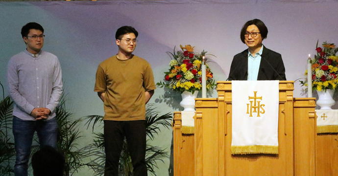 During a young adult worship service at First Korean United Methodist Church in Wheeling, Ill., on June 13, Jinho Woo introduces two young members who are moving to other areas for jobs or schools. They were encouraged to serve Christ in their new places. Photo by the Rev. Thomas Kim, UM News.