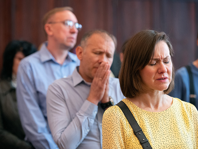 Maryna Tagunkova (front) and Eduard Holtman (center) join in prayer at Prague 2 United Methodist Church. They are members of Agapé United Methodist Church, the Russian-speaking congregation that shares space with the Czech-speaking congregation. Holtman is a lay speaker at the church and regularly drives relief supplies to the Ukrainian border. Photo by Mike DuBose, UM News. 