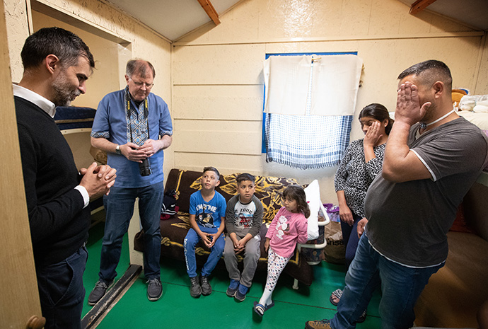 The Revs. László Khaled (left) and Üllas Tankler (second from left) pray with the family of Robert, Renatta and their children in the small cabin they share at the United Methodist Dorcas church camp in Debrecen, Hungary, in May. The family was staying after fleeing the war in Ukraine. Khaled is superintendent of The United Methodist Church in Hungary and Tankler is the European/Eurasian representative of the United Methodist Board of Global Ministries. File photo by Mike DuBose, UM News.