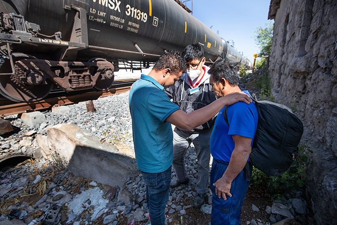 The Rev. Joel Hortiales (center) prays with migrants Darwin (left) and Santiago as they wait for a southbound train to pass behind the Oasis en el Medio del Camino migrant shelter in Apaxco, Mexico, in April. Hortiales, a United Methodist missionary and director of Hispanic-Latino ministries and border concerns for the California-Pacific Conference of The United Methodist Church, was part of a fact-finding ministry that visited the shelter, which is operated by the Methodist Church of Mexico with support from the United Methodist Committee on Relief. File photo by Mike DuBose, UM News.