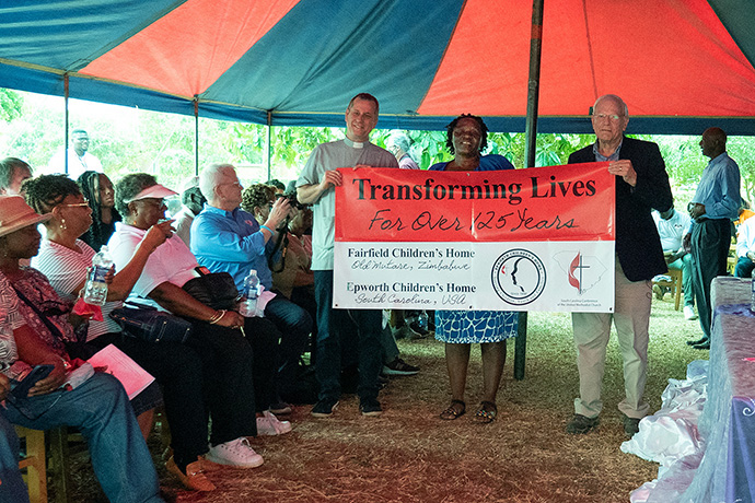 The Rev. Owen Ross (left) holds a banner alongside the Revs. Juliet Mwarumba and John Holler during a ceremony celebrating a $800,029 donation to Fairfield Children’s Home in Mutare, Zimbabwe. Ross and Holler, who are from the North Texas and South Carolina conferences, respectively, have personal connections to the school. Mwarumba is Fairfield’s administrator. Photo by Kathy L. Gilbert.