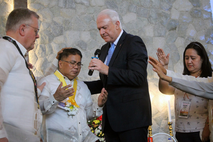 Bishops Christian Alsted (left) and Thomas J. Bickerton pray for newly elected Bishop Rodel M. Acdal after he received his episcopal pin during the Philippines Central Conference at Wesleyan University-Philippines in Cabanatuan City, Philippines. On the right is Acdal’s wife, Maria Rosario Cherry Acdal. Delegates to the conference elected Acdal on the sixth ballot on Nov. 25. Photo by Gladys P. Mangiduyos, UM News.