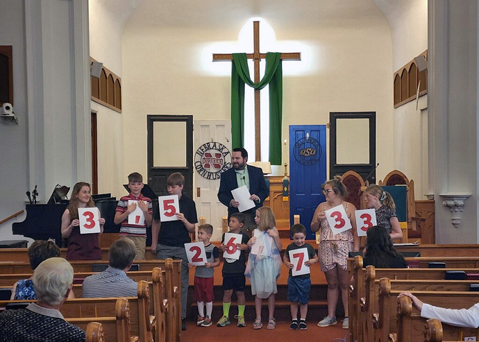 The Rev. Michael Carpenter, pastor of Wahoo First United Methodist Church in Nebraska, looks on as children from the church display the amount of medical debt ($3,526,733) the congregation helped pay off through its RIP Medical Debt campaign. Photo courtesy of Wahoo First United Methodist Church. 