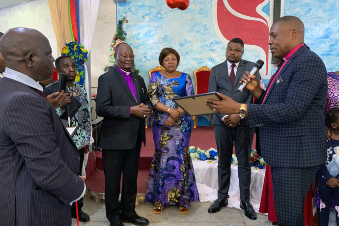 L’Évêque Daniel Lunge, à droite, présente le diplôme d’excellence décerné à l’Evêque Unda par l’association des enfants des pasteurs pour ses 50 ans de sacerdoce et pour les 100 ans de l’Église Méthodiste Unie au Congo Est. Photo du Pasteur Fiston Okito, UM News.