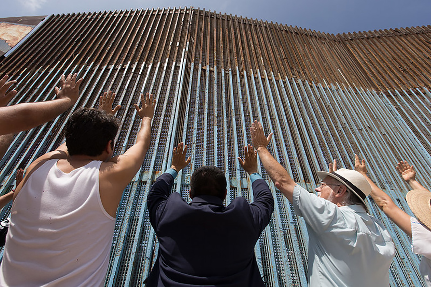 The Revs. Joel Hortiales (center, in blue blazer) and David Farley (to Hortiales' right) join parishioners of the Border Church in Tijuana, Mexico, as they lift their arms skyward beneath the fence that marks the border with the U.S. Photo by Mike DuBose, UM News.