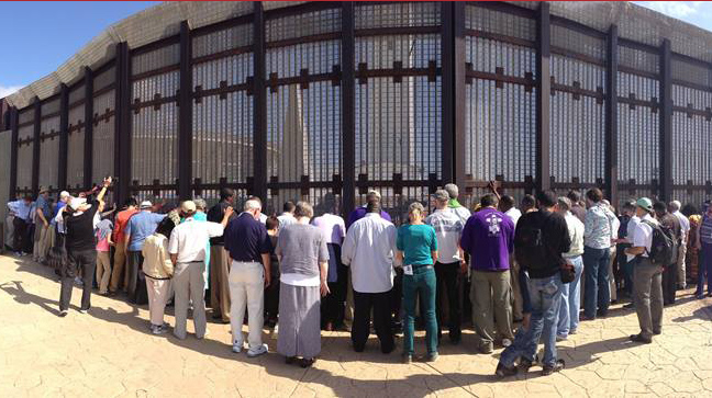 In May 2013, United Methodist bishops from around the world visited the U.S. border with Mexico. In this file photo, the bishops raise their hands in prayer together in Friendship Park on the U.S. side, while another group of leaders from the border community, from the Methodist Church of Mexico and relatives of immigrants, do the same on the Mexican side from Parque El Faro in Tijuana. File photo by David Valera, UM News.