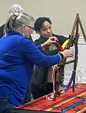 The Rev. Nancy Tomlinson, a district superintendent in the Great Plains Conference, and KMarie Tejeda, a student at the Boston University School of Theology, tie ribbons on a Native American dreamcatcher in a show of respect for Native Americans at the Best Western Plus Saddleback Inn and Conference Center in Oklahoma City on March 12, 2023. Photo by Jim Patterson, UM News.