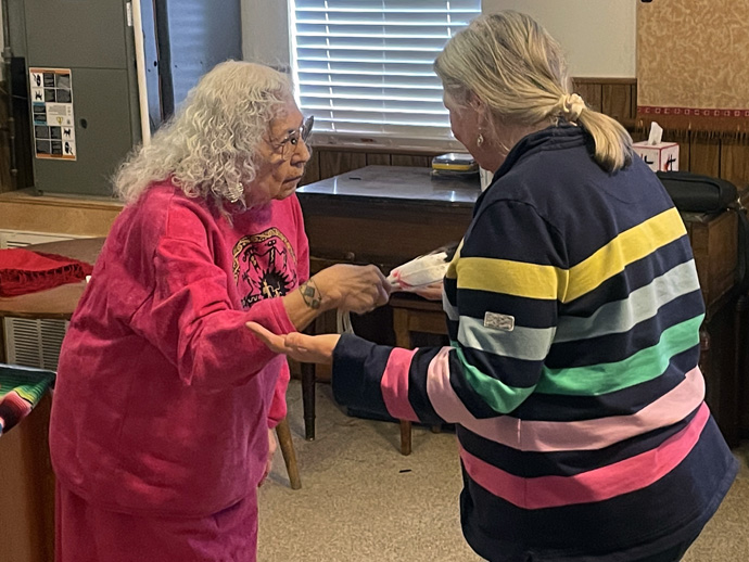 Henrietta Mann, a retired college professor, Native American activist and Cheyenne prayer woman, performs a smudging ceremony on the Rev. Nancy Tomlinson, a district superintendent in the Great Plains Conference. The ceremony, performed on March 10, 2023, at the Clinton Indian Church and Community Center in Clinton, Okla., is used to cast out negativity while also putting protection around a person to ward off threats. Photo by Jim Patterson, UM News.