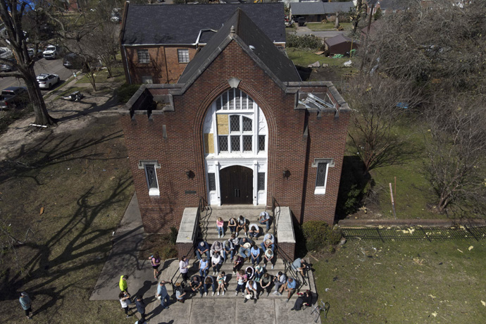 People worship on the steps of Rolling Fork United Methodist Church amid visible debris from surrounding properties on March 26, in Rolling Fork, Miss. Tornadoes tore through the state on the night of March 24 destroying buildings and knocking out power. (AP Photo/Julio Cortez)
