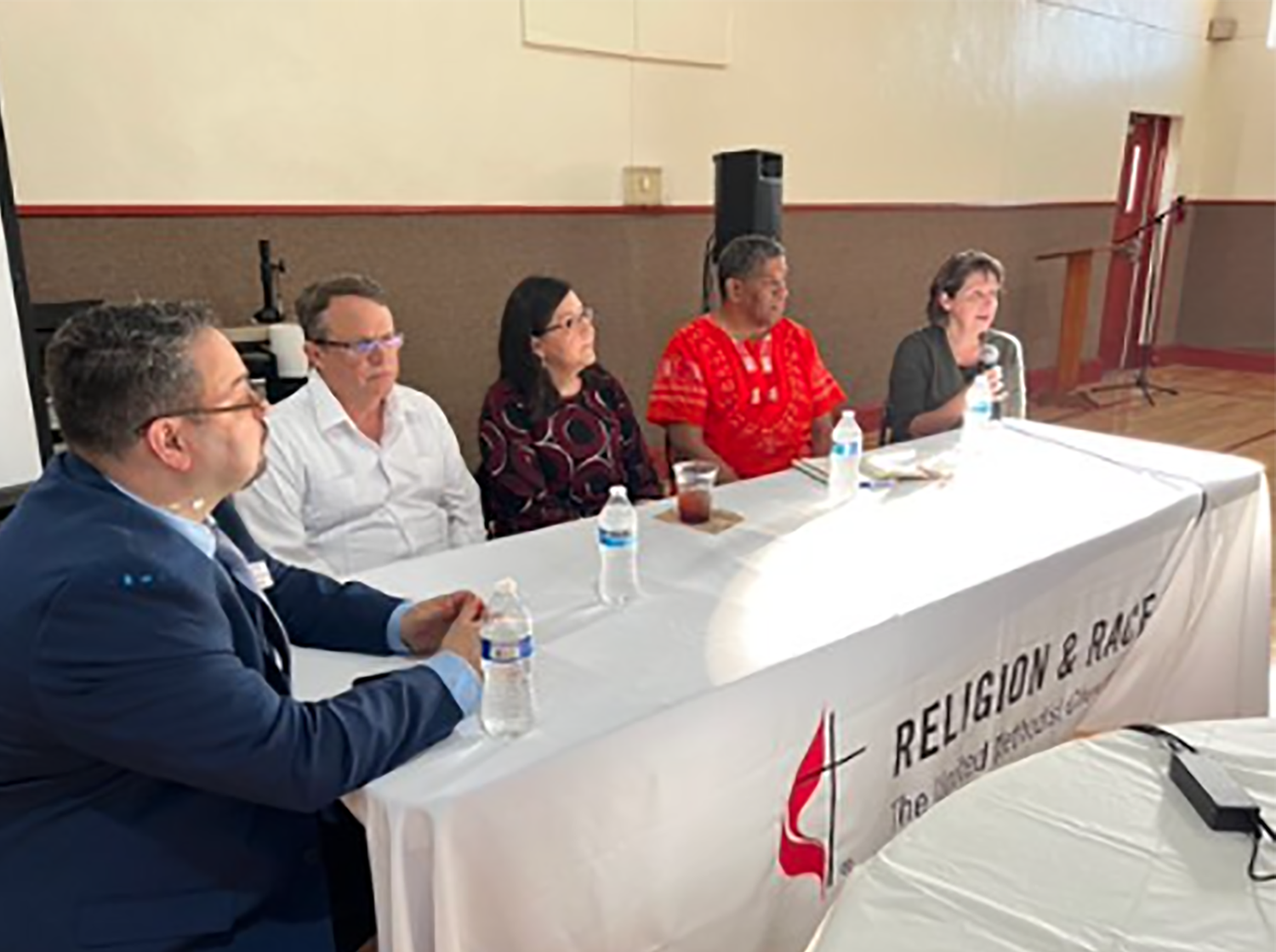 El Rev. Dr. Giovanni Arroyo secretario general de GCORR, al extremo izquierdo, dirige un panel de discusión con los/as reverendos/as John Feagins, Raquel Feagins, James Amerson y Cynthia Engstrom, de izquierda a derecha. Foto cortesía de GCORR.