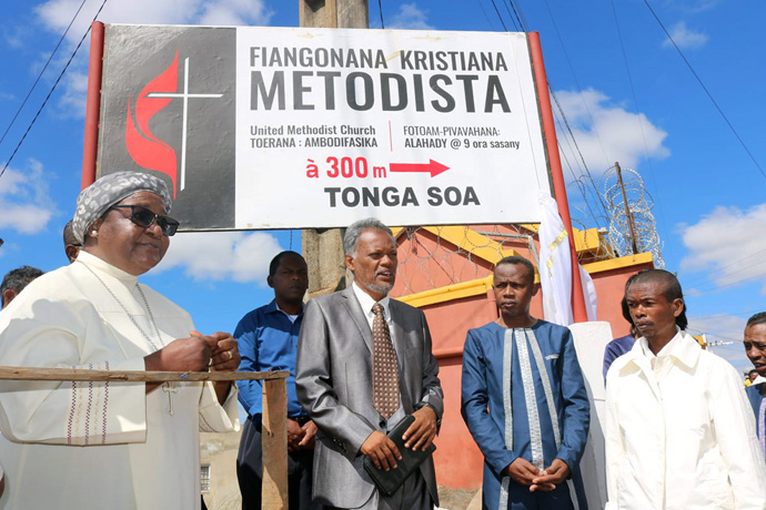 A Bispa Joaquina Filipe Nhanala (à esquerda) ao lado de Ratovohery Jean Aime (segurando a Bíblia) durante a instalação da sinalização direcional para a Igreja Metodista Unida Ambodifasika em Madagascar. A placa, doada pelas Comunicacoes da Metodista Unida, foi inaugurada durante a viagem da bispa em Fevereiro. Foto de Alvin Makunike, Noticias da MU.