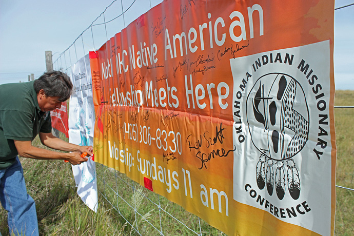 Bishop David Wilson, then conference superintendent of the Oklahoma Indian Missionary Conference of The United Methodist Church, attaches banners from his conference to a fence near the Dakotas Access Pipeline, Highway 1806, near Cannon Ball, N.D., in 2016. File photo by Dave Stucke, Dakotas Conference.