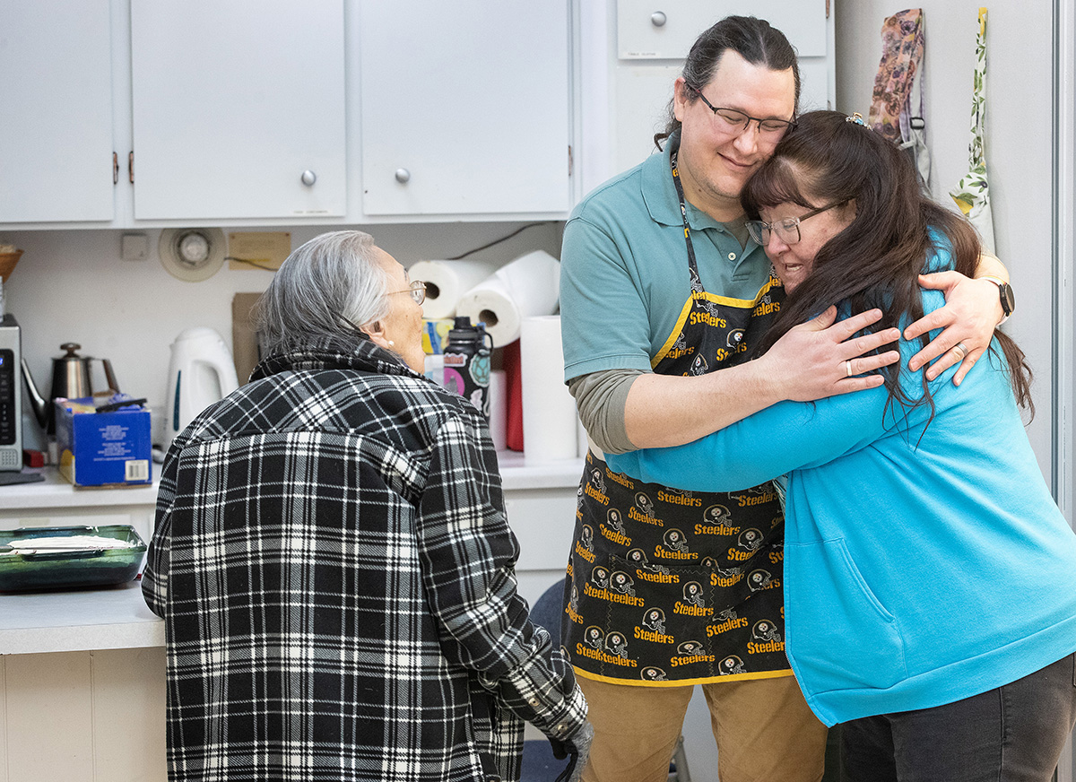 Nina Gorman (à direita) abraça o Rev. Murray Crookes na cozinha da Igreja Metodista Unida de Todas as Nações em Anchorage, Alasca, onde Crookes e a sua família organizam uma refeição semanal de comunhão e estudo bíblico. Foto de Mike DuBose, Notícias MU.
