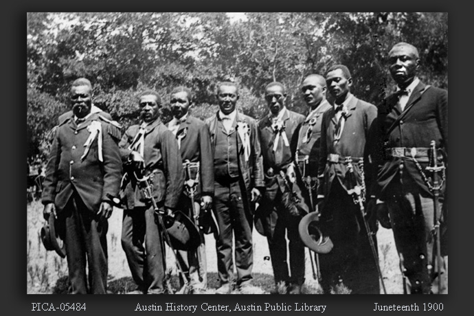 Eight men in suits with ceremonial swords on their hips, June 19, 1900. These were the "officers of the day" at the Emancipation Day Juneteenth celebration. The ceremony was held at East Woods park on East 24th Street. Mrs. Stephensen kept a diary of the day, which she later sold to the San Francisco Chronicle. Photo by Grace Murray Stephenson, courtesy of the Austin History Center, Austin Public Library.