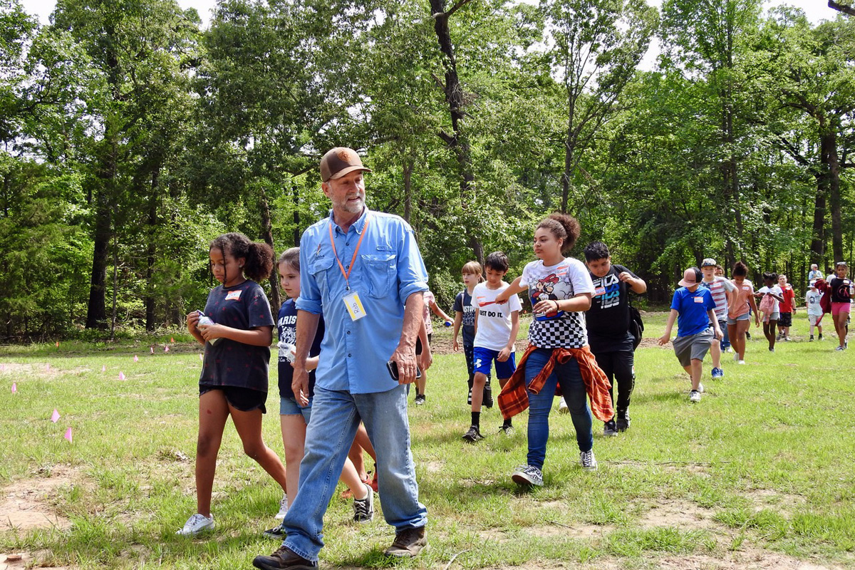 The Rev. Rob Spencer leads a group of Paris, Texas, schoolchildren at Methodist Camp on Pat Mayse Lake. Spencer, a longtime United Methodist elder, is the fulltime leader of Cultiv8 Community, a nonprofit he started that has a goal of getting kids into nature more. This group from Justiss Elementary was at the camp on May 19, and planted milkweed seedlings to improve habitat for monarch butterflies. Photo by Sam Hodges, UM News.