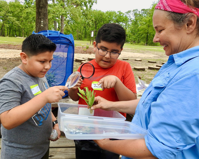 As Cultiv8 Community camp director Ashlea Mattoon looks on, Allan Castillo (left) and Jacob Coronado examine a monarch butterfly caterpillar. The boys were part of a Paris, Texas, elementary school group that spent most of May 19 at the Methodist Camp on Pat Mayse Lake, near Paris. Photo by Sam Hodges, UM News.