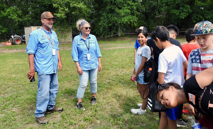 The Rev. Rob Spencer and Celeste Spencer, his wife, talk with kids from Justiss Elementary of Paris, Texas, on May 19 at Methodist Camp on Pat Mayse Lake. The kids dug holes and planted and watered native wildflower seedlings that are host plants for butterflies. Photo by Sam Hodges, UM News.