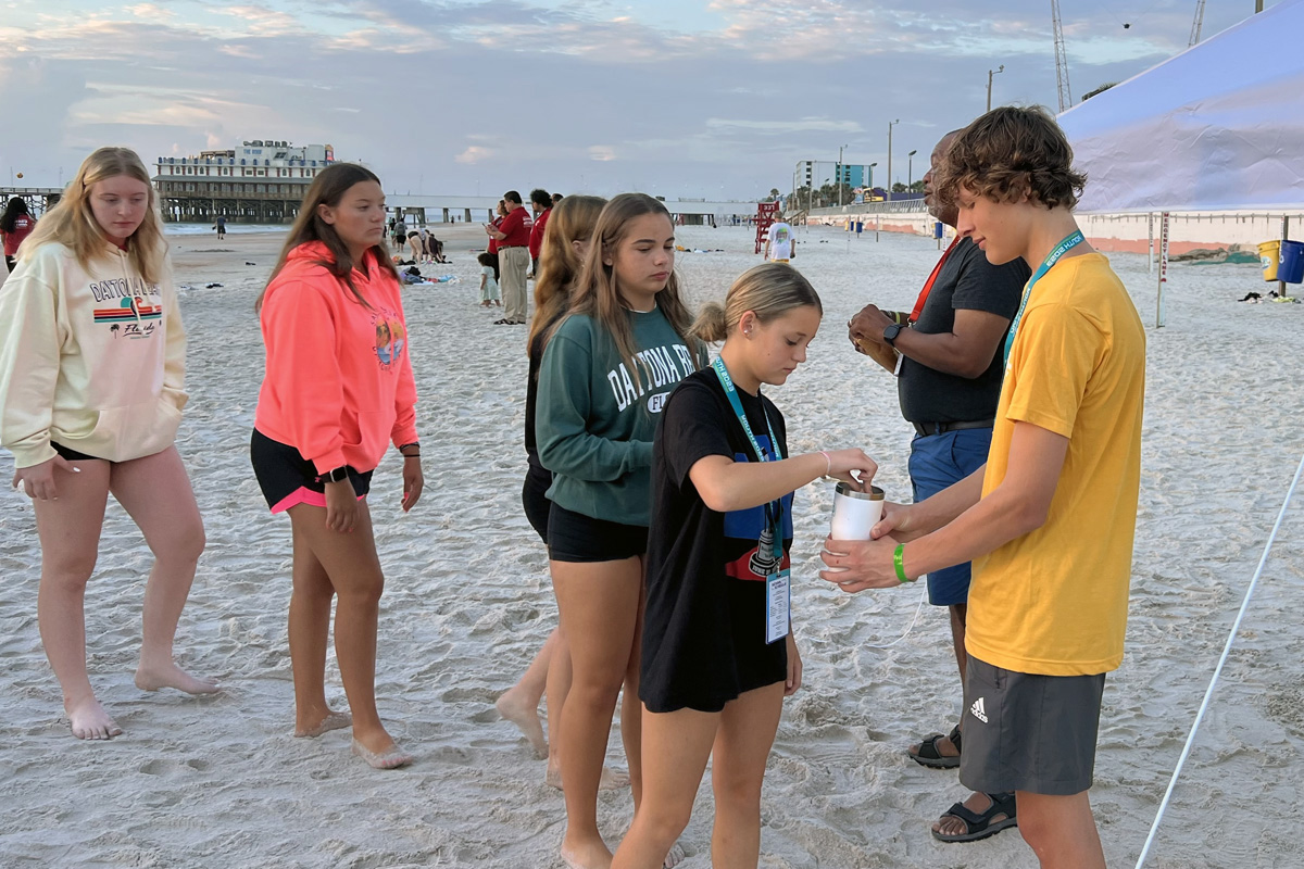Tessa Brunner from First United Methodist Church in Chanute, Kan., receives communion from Eli Hodge, youth volunteer at Lebanon United Methodist Church in Lebanon, Tenn., during sunrise communion at Youth 2023 in Daytona Beach, Fla. Photo by Crystal Caviness, United Methodist Communications.