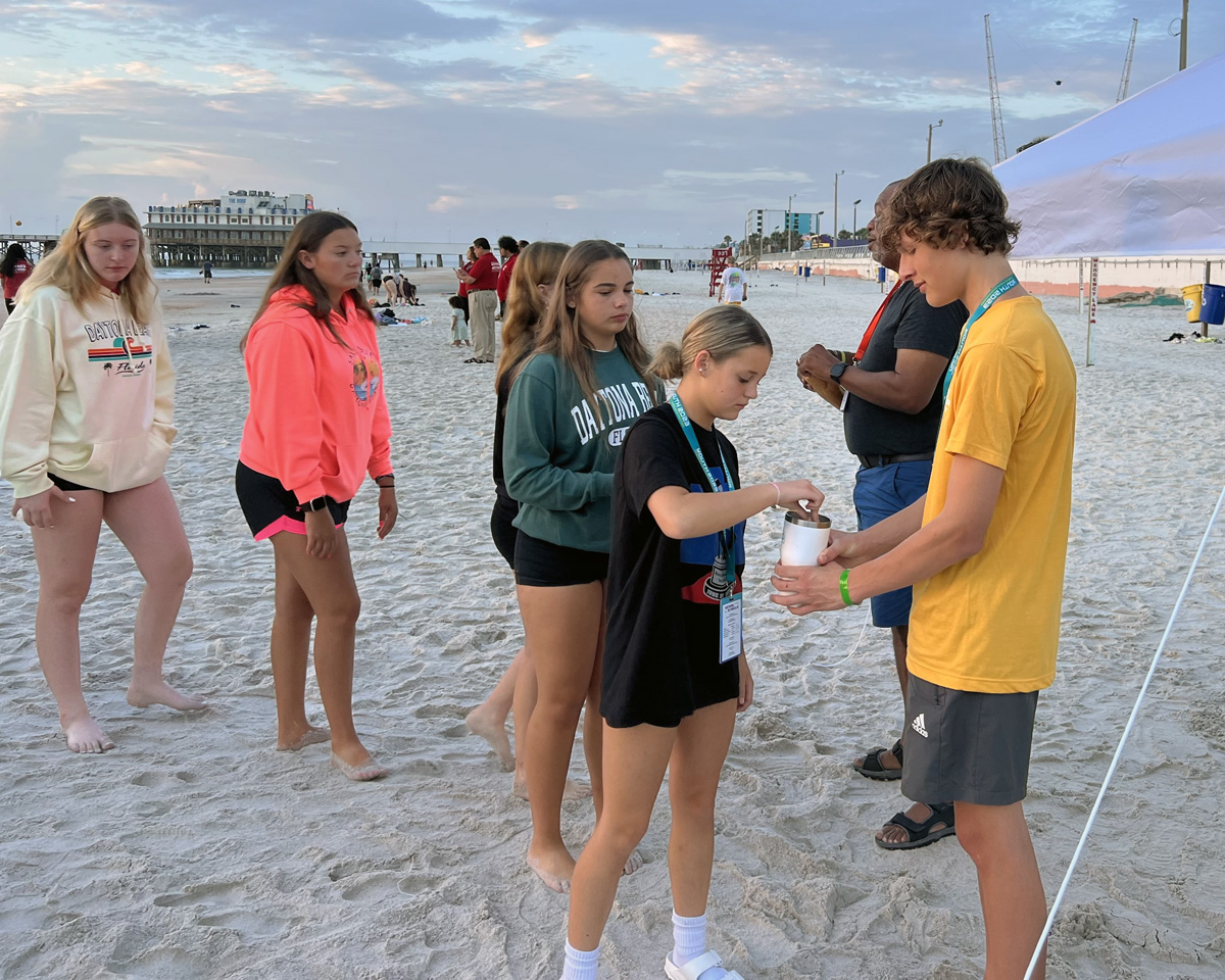 Tessa Brunner from First United Methodist Church in Shinute, Kan., receives communion from Eli Hodge, youth volunteer and member of Lebanon United Methodist Church in Lebanon, Tenn., during sunrise communion at Youth 2023 in Daytona Beach, Fla. More than 2,500 attended the quadrennial youth event July 25-28. Photo by Crystal Caviness, United Methodist Communications.