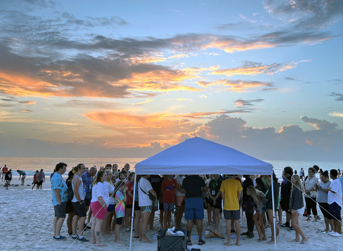 Dozens gather under a tent for communion at sunrise during Youth 2023 held in Daytona Beach, Fla., July 25-28. Representatives from 12 of the 13 agencies of The United Methodist Church participated as speakers, workshop leaders and exhibitors. Photo by Crystal Caviness, United Methodist Communications.