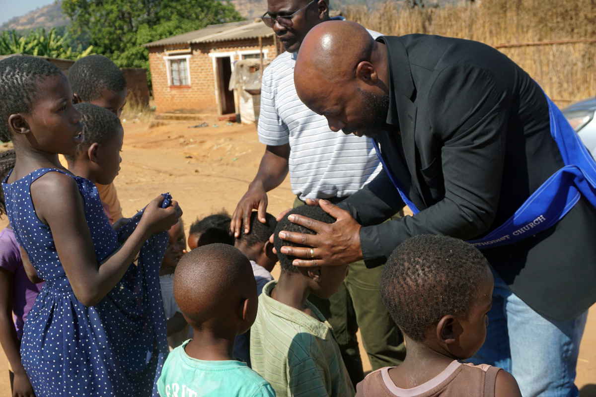 Elison Mukandi (black jacket) and Samuel Muchemwa (striped shirt) lay hands on children wishing to be prayed for at Chipunza Farm in Harare, Zimbabwe, in June. The men’s organization of Chisipiti United Methodist Church launched “Vhuserere,” an evangelism effort to reach people in farming areas. Mukandi is chairperson of the men’s group. Photo by Kudzai Chingwe, UM News.