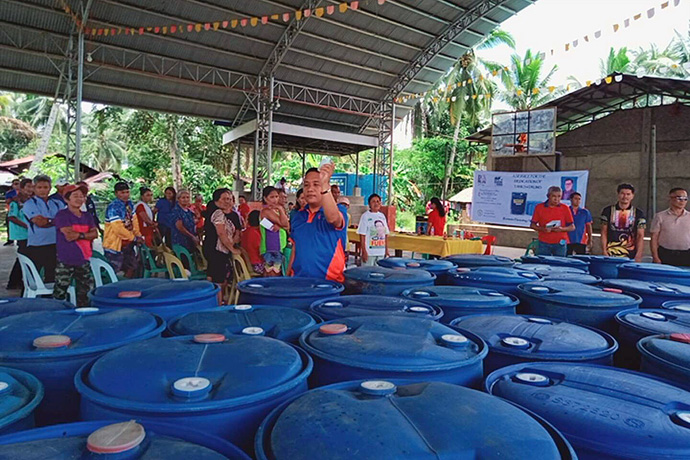 The Rev. Mark Kevin O. Nebran of the North East District of East Mindanao blesses rainwater-harvesting drums to be distributed in the Novele community in the Philippines as some recipients look on. The Davao Area’s disaster management team distributed the drums to more than 30 families. Photo courtesy of the Rev. Dan Reuben L. Sison.