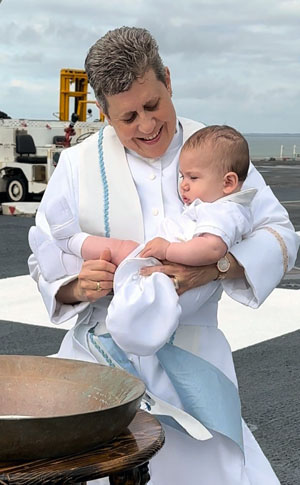 Commander Genevieve Clark performs a "bell" baptism in late April on the flight deck of the USS Gerald R. Ford in Norfolk, Va., prior to deployment. In Naval tradition, the ship's bell is inverted and used as the baptismal font and then all souls baptized from the bell's water have their names engraved inside the bell. Photo courtesy of Genevieve Clark.