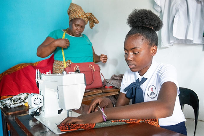 A estudante Luiza Monjane pratica a costura como parte dum programa de formação profissional para raparigas e mulheres no Centro de Treinamento da Metodista Unida em Tsalala, perto de Maputo, Moçambique. Atrás está Glória Julião, estudante adulta do programa. Foto de Mike DuBose, Notícias da MU. 