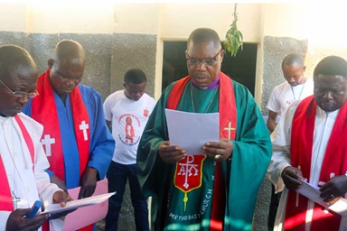 Bishop Daniel O. Lunge, resident bishop of the Central Congo Area, delivers a prayer of dedication at a new United Methodist church in the Nkonko camp for displaced persons in Kananga, Congo. He is surrounded by United Methodist leaders from the Kinshasa District and Kasai Annual Conference. The camp houses Congolese who were expelled from Angola after they fled to that country in 2017 amid insecurity. Photo by Cédrick Okandjo, UM News.