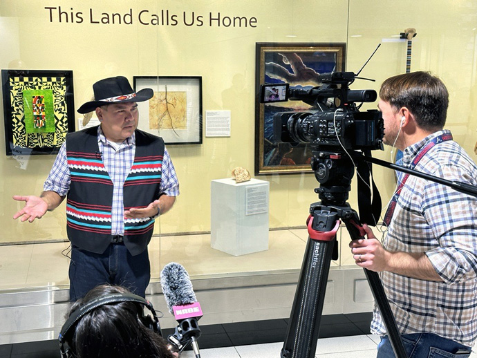 The Rev. Chebon Kernell (Seminole/Muscogee), executive director of the Native American Comprehensive Plan of The United Methodist Church, speaks with a reporter at the opening of “This Land Calls Us Home,” held at Hartsfield-Jackson Atlanta International Airport in Atlanta on Nov. 6. Photo by Susan Clark, courtesy of Global Ministries.