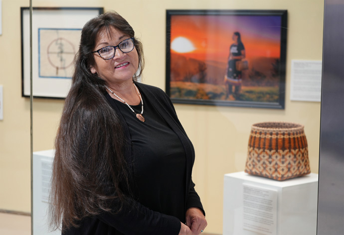 Artist Vivian Garner Cottrell (Cherokee) stands near a display case that features one of her baskets at the opening of “This Land Calls Us Home” held at Hartsfield-Jackson Atlanta International Airport in Atlanta on Nov. 6. Photo courtesy of Global Ministries.