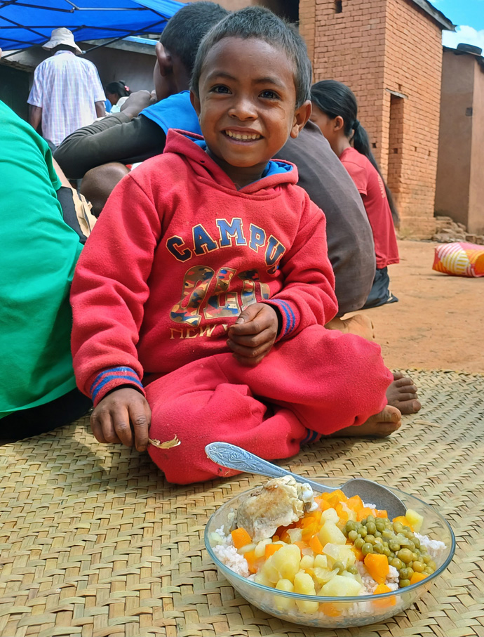 Un garçon sourit après avoir reçu une assiette pleine de nourriture dans le village de Faratanjona à Madagascar. Les membres de l’Église Méthodiste Unie d’Ambodifasika à Antananarivo sont allés dans cette région éloignée pour livrer de la nourriture et d’autres formes de soutien à la communauté. Photo d’Esdras Rakotoarivony, UM News. 