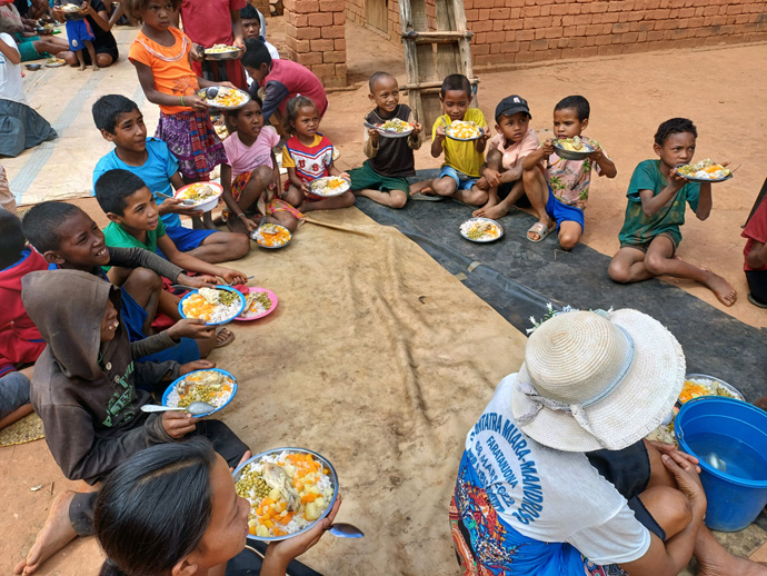 Children in Faratanjona sit on a tarp before partaking in a meal provided by Ambodifasika United Methodist Church. Members of the Antananarivo church traveled to the remote village to deliver food and share the gospel. In the absence of schools or open spaces for communal meals in this rural area, families set up a makeshift dining area near the preaching site. Photo by Esdras Rakotoarivony, UM News.