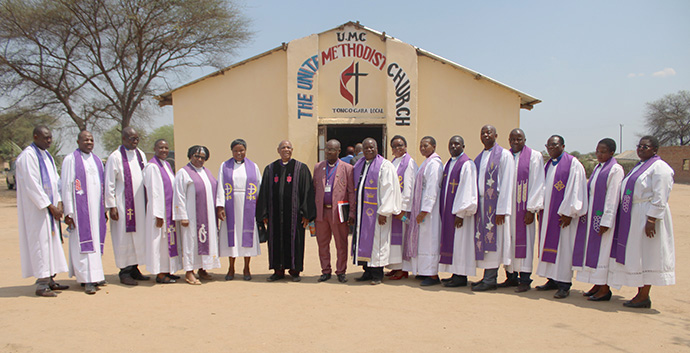 L’évêque Eben K. Nhiwatiwa (en robe noire) et les membres de son cabinet se rassemblent pour une photo devant le temple de l’Église Méthodiste Unie construit par des réfugiés et des demandeurs d’asile au camp de réfugiés de Tongogara. Photo de Kudzai Chingwe, UM News. 