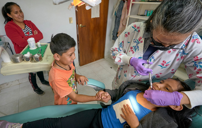 Dentist Ivon Garcia operates on 6-year-old Yaretzi Valencia, who gets moral support from her brother, 8-year-old Jose Miguel, in a clinic run by the Methodist Church of Mexico in the village of San Andrés Tlalamac, Mexico. The children's mother, Norma Valenica, observes in the background. The clinic was built by volunteer groups from the United States, but the local community — hard hit by climate change — has had difficulty keeping it open. The project has received support from the United Methodist Board of Global Ministries. Photo by the Rev. Paul Jeffrey, UM News.