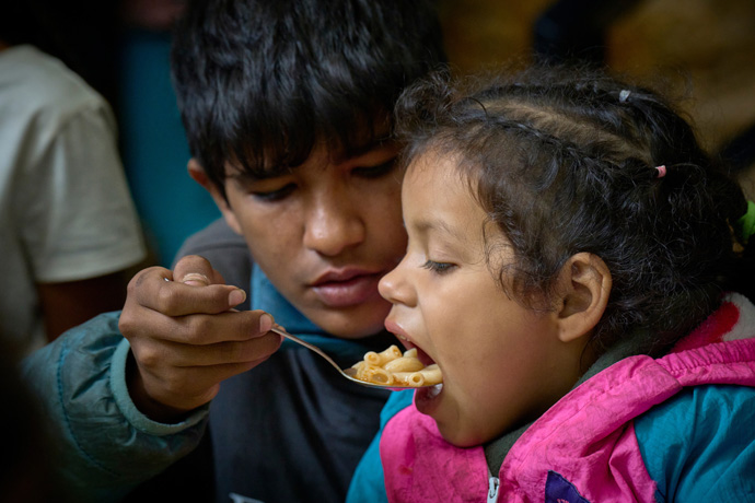 Wilbur, a 15-year old boy from Venezuela, helps his 5-year-old sister, Noemi, eat a meal in the Center for Attention to Migrants, a shelter housed in the Holy Trinity Methodist Church in Apaxco, Mexico. The center provides food, medical care, clothing, a safe place to sleep, showers, free phone calls back home and spiritual counseling to hundreds of migrants a day. The center receives support from the United Methodist Committee on Relief. Photo by the Rev. Paul Jeffrey, UM News.
