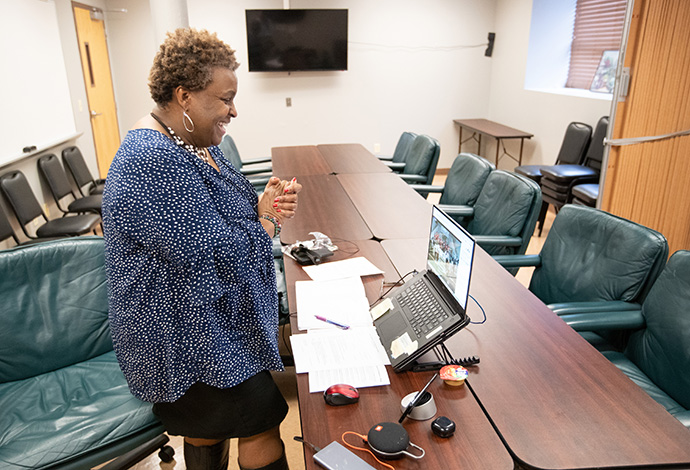 Tina Boone stands to join in singing the opening hymn, “Lift Every Voice and Sing,” from her post in a conference room at Gordon Memorial United Methodist Church in Nashville, Tenn. She uses her cell phone, connected to the church’s conference line, to share audio from the Facebook livestream of worship and to help callers understand what’s happening on the video feed, which they can’t see. Photo by Mike DuBose, UM News.