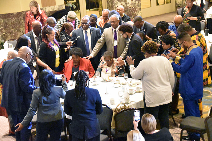 Bishop Gregory Palmer (standing), surrounded by BMCR General Meeting attendees, prays a benediction over (seated from left) closing speaker Stacey Abrams and her mother, the Rev. Carolyn Abrams, a retired United Methodist clergywoman. Photo by John Coleman, UM News.